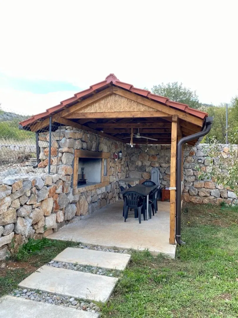 Covered gazebo with a built-in barbecue and seating set in the yard.