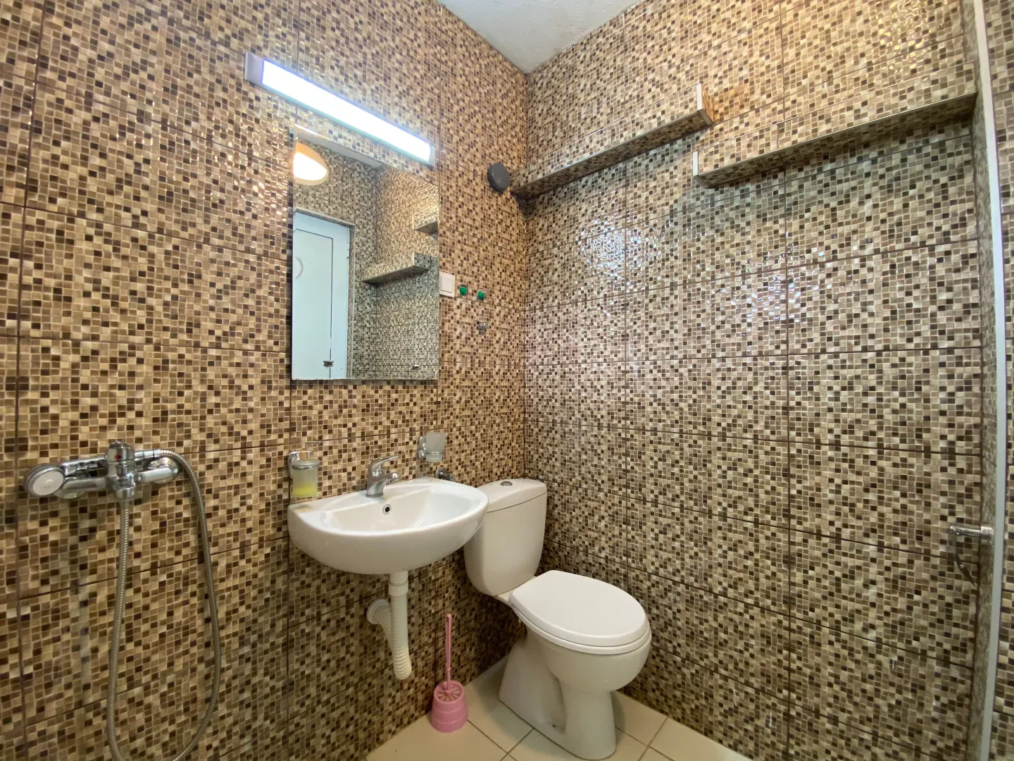 Bathroom lined with mosaic tiles featuring a washbasin, mirror, and toilet.