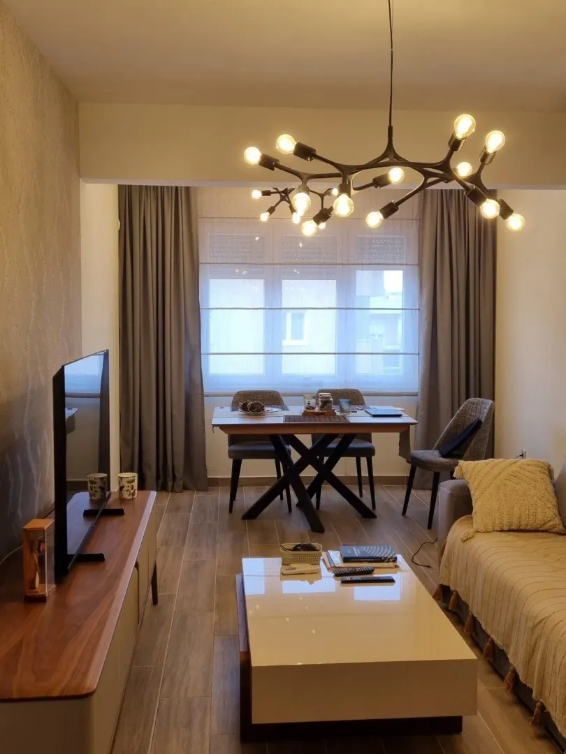 Svijetao dnevni boravak sa trpezarijskim stolom i modernim lusterom.