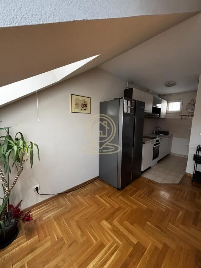 Small attic kitchen with wooden parquet flooring and a refrigerator.