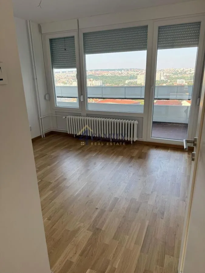 Prazna soba sa drvenim podom i velikim prozorima koji nude pogled na grad.