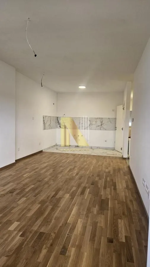 Empty room with wooden flooring and a prepared kitchen area.