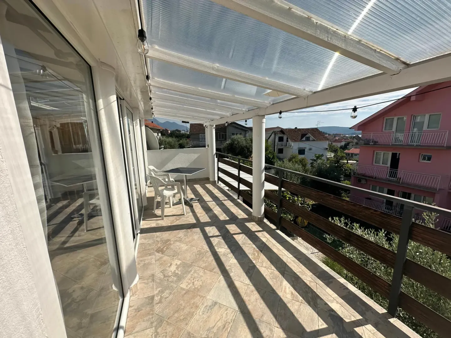 Covered terrace with a table, chairs, and a view of surrounding houses.