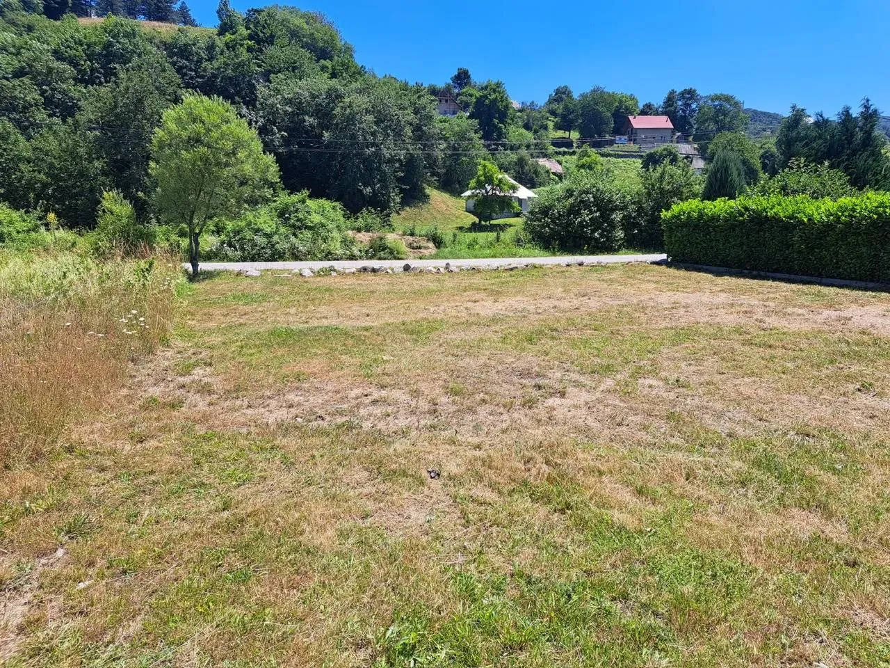 Prostran i ravan travnati plac okružen zelenilom i drvećem.