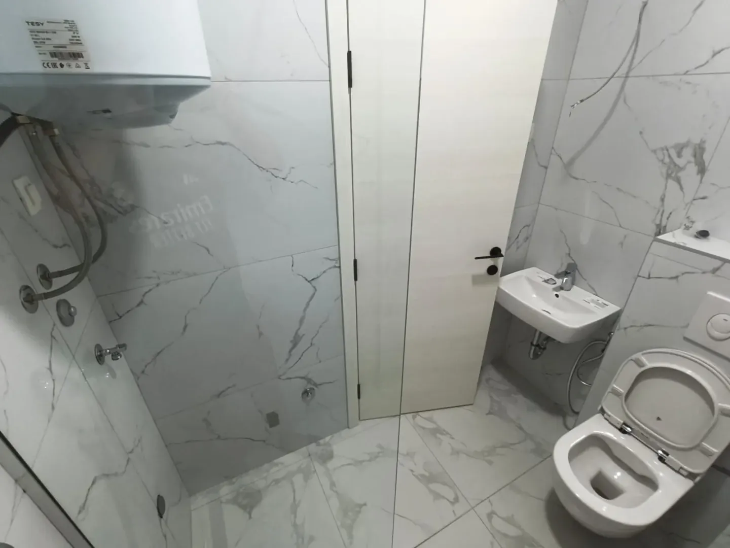 Manje kupatilo obloženo mermernim pločicama sa wc šoljom, umivaonikom i bojlerom.