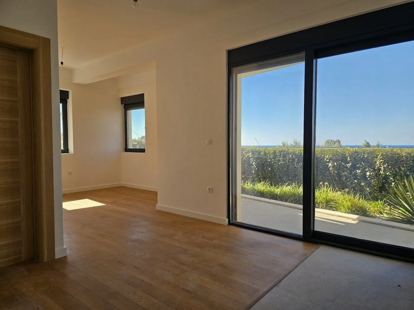 Empty living room with wooden flooring and large glass balcony doors.