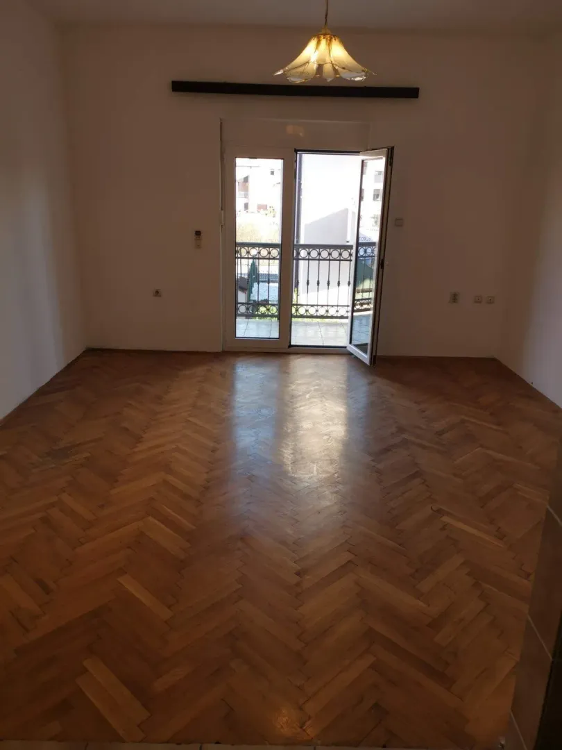 Prazna soba sa parketom i izlazom na balkon.