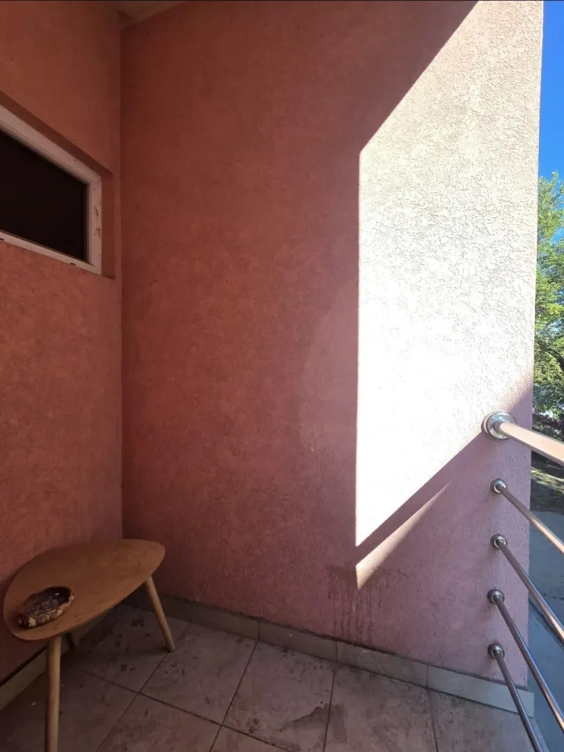 Manji namješteni balkon sa drvenim stolićem i metalnom ogradom.
