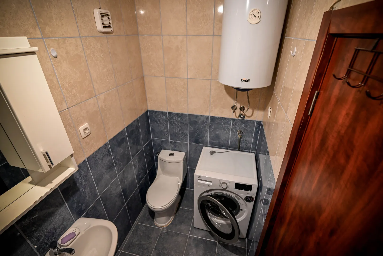 Manje kupatilo sa WC šoljom, umivaonikom i veš mašinom.