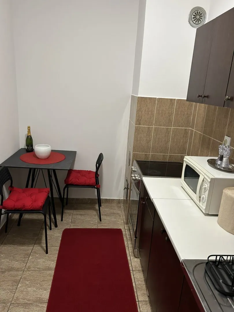 Mala kuhinja sa trpezarijskim stolom i crvenim detaljima.