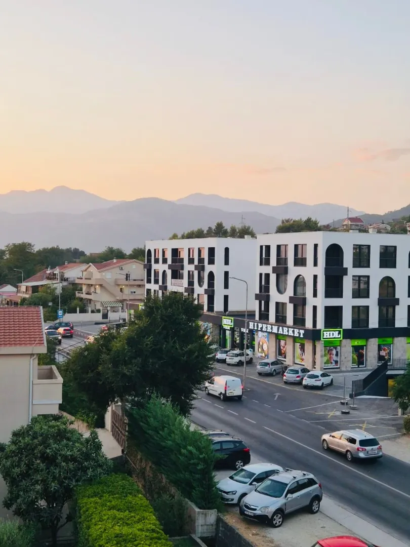 View from the apartment overlooking the street, modern building, and surrounding mountains.