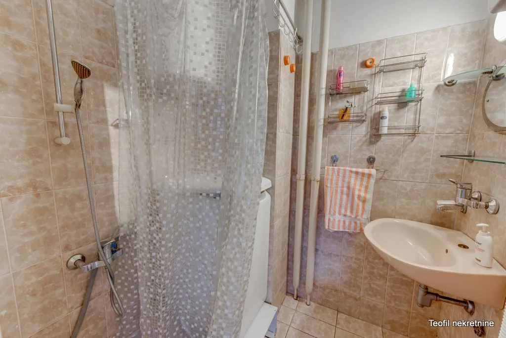 Small bathroom with a shower enclosure, washbasin, and beige tiles.