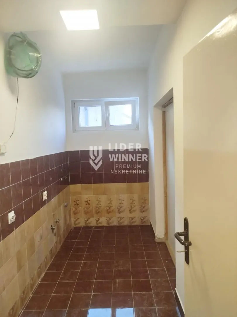 Empty tiled kitchen with a window and utility connections.
