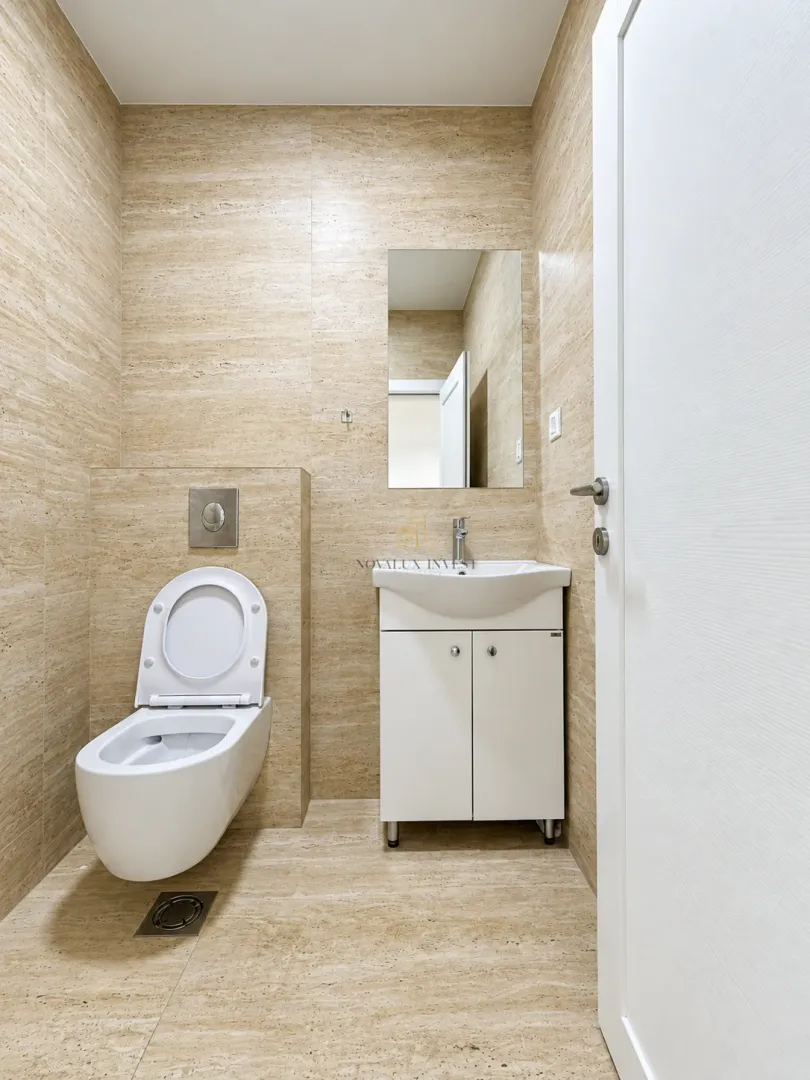 Small bathroom with a toilet, washbasin, and mirror finished with beige tiles.