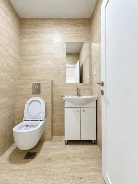 Small bathroom with a toilet, washbasin, and mirror finished with beige tiles. - image 11