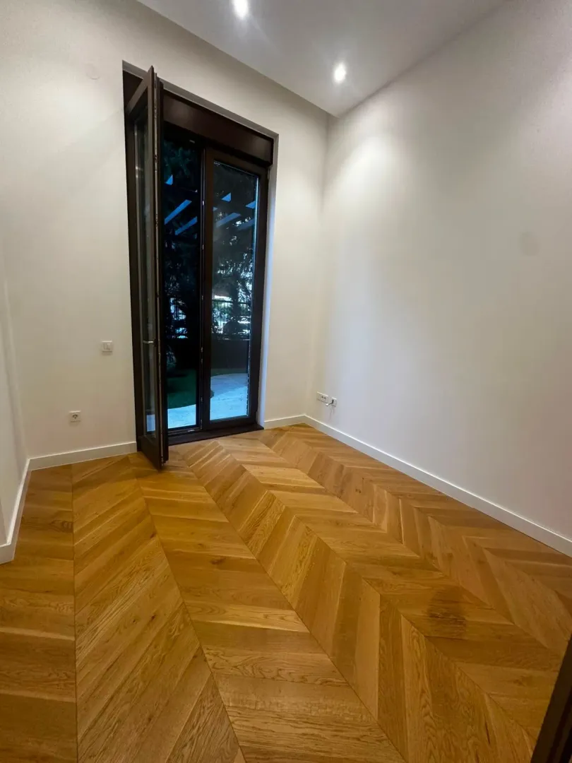Prazna soba sa drvenim parketom i balkonskim vratima.