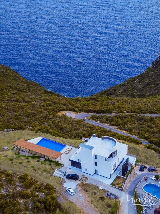 Aerial view of a villa with a swimming pool located near the seashore.