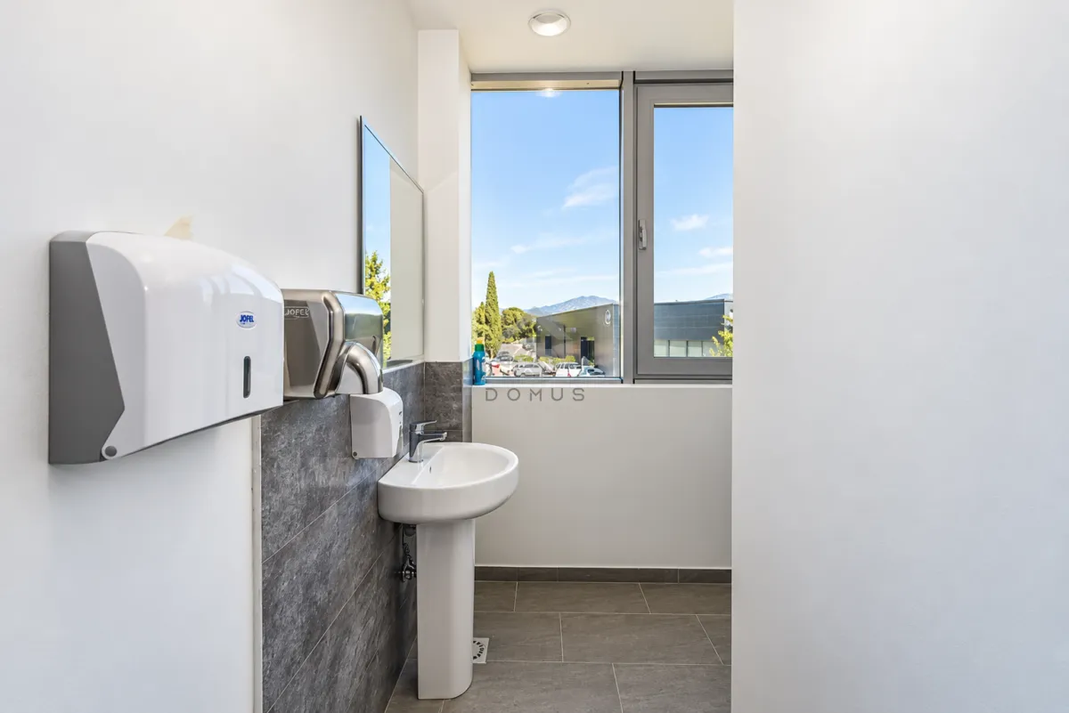 View of the sink and soap dispensers in a modern bathroom with a large window.