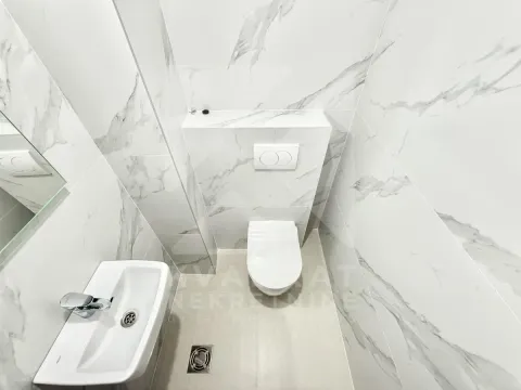 Smaller bathroom with white marble-pattern tiles, a washbasin, and a toilet. - image 10