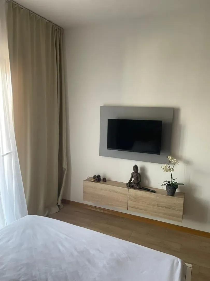 Uređena spavaća soba sa krevetom, TV-om na zidu i visećom komodom.