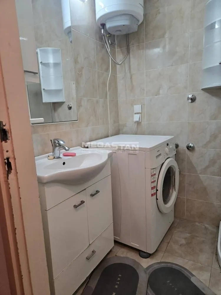 Kupatilo opremljeno umivaonikom, veš mašinom i pločicama.