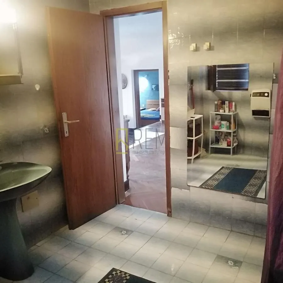 Kupatilo sa umivaonikom, ogledalom i otvorenim vratima prema hodniku.