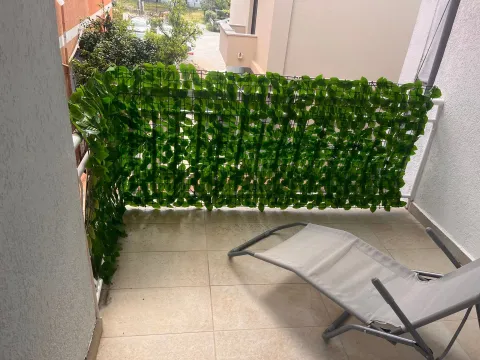 Balkon sa ogradom ukrašenom vještačkim lišćem i ležaljkom. - image 7