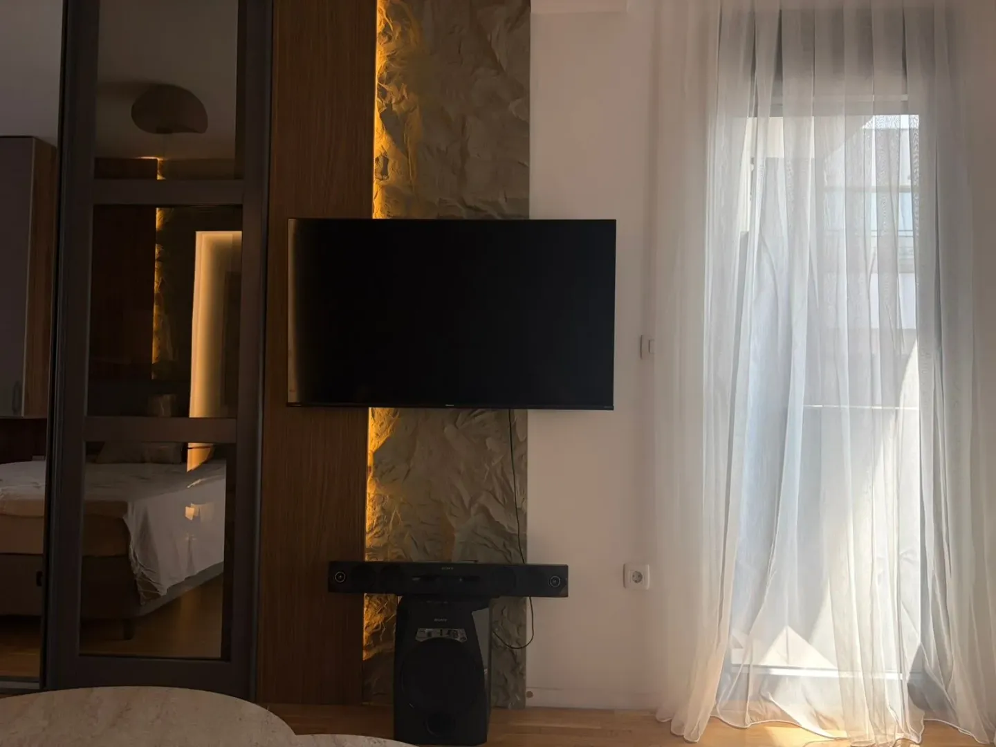 Dnevna soba sa televizorom i dekorativnim kamenim zidom.