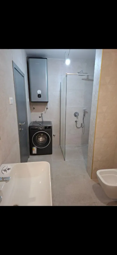 Moderne kupatilo sa tuš kabinom, umivaonikom i mašinom za veš.