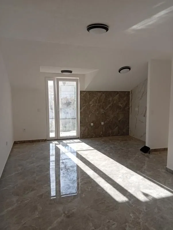 Prazna soba sa pločicama na podu i izlazom na balkon.