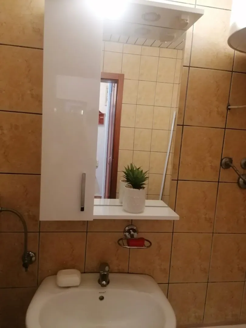 Manje kupatilo sa umivaonikom, ogledalom i braon pločicama.
