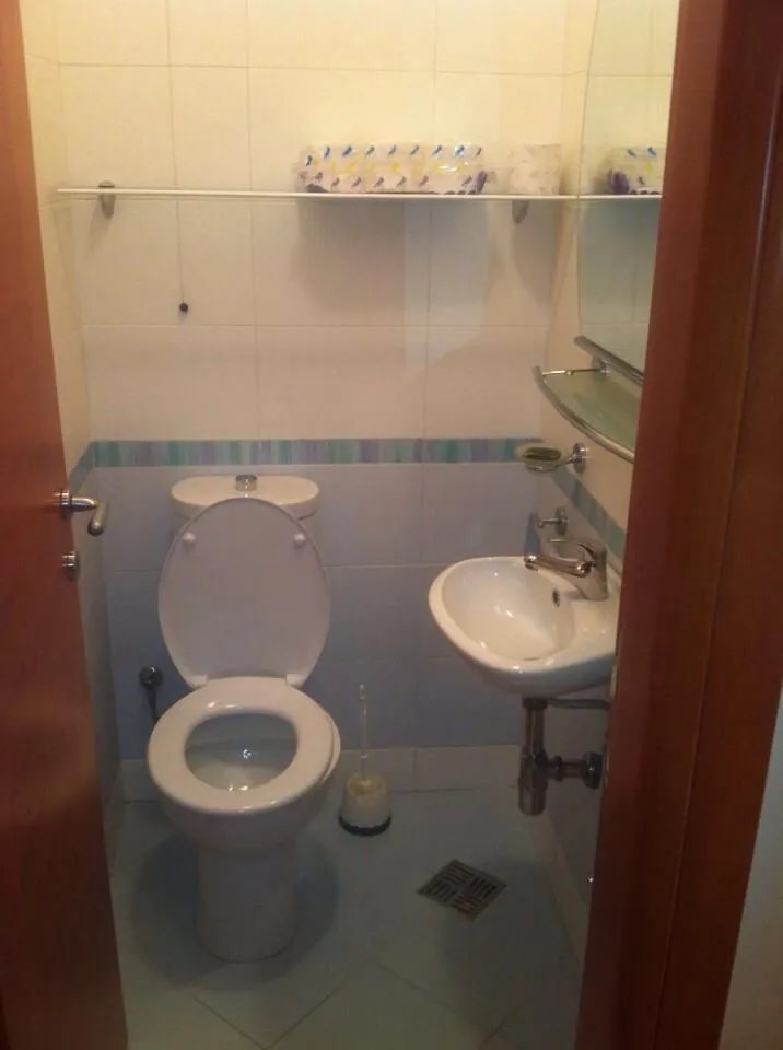 Malo kupatilo sa toaletom i lavaboom, fotografisano kroz otvorena vrata.