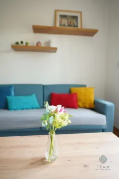 Living room with a blue sofa and a wooden coffee table with a vase of flowers. - image 4