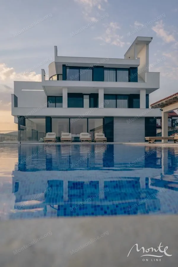 View of a modern villa with a swimming pool and sun loungers in the yard.