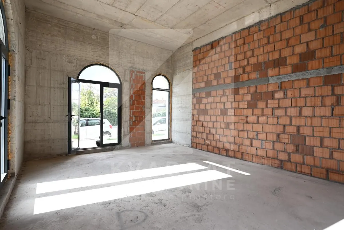 Unfinished room in grey construction phase with large arched windows and daylight.