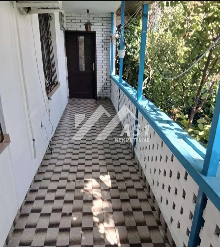 Natkriveni balkon sa popločanim podom i plavom ogradom.