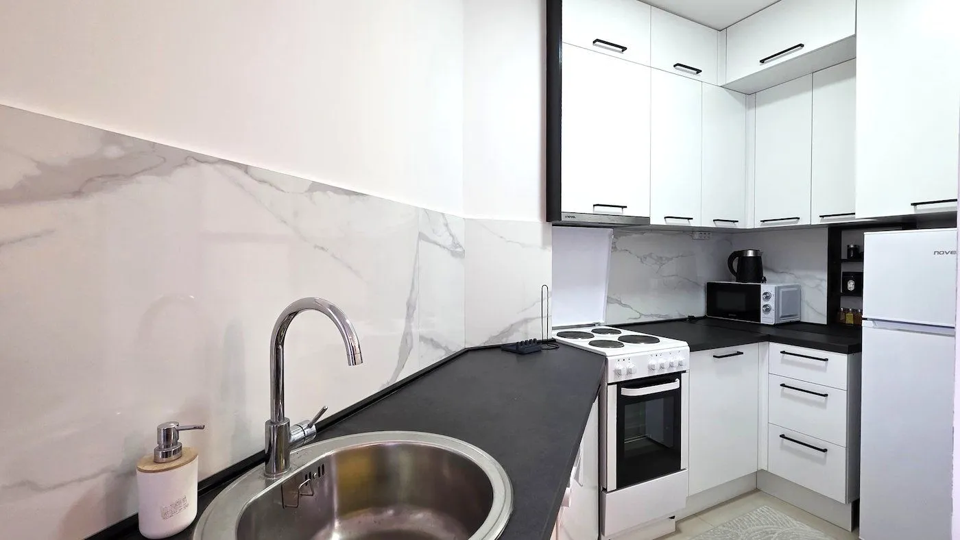 Modern kitchen with white cabinets, black countertop, and a sink in the foreground.