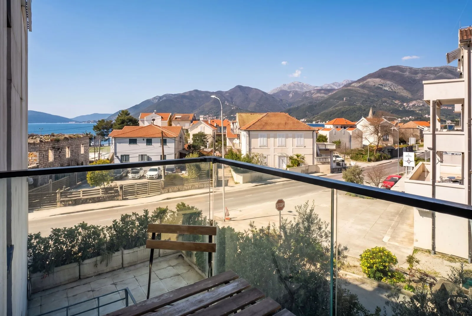 Pogled sa balkona na more, planine i okolne kuće.
