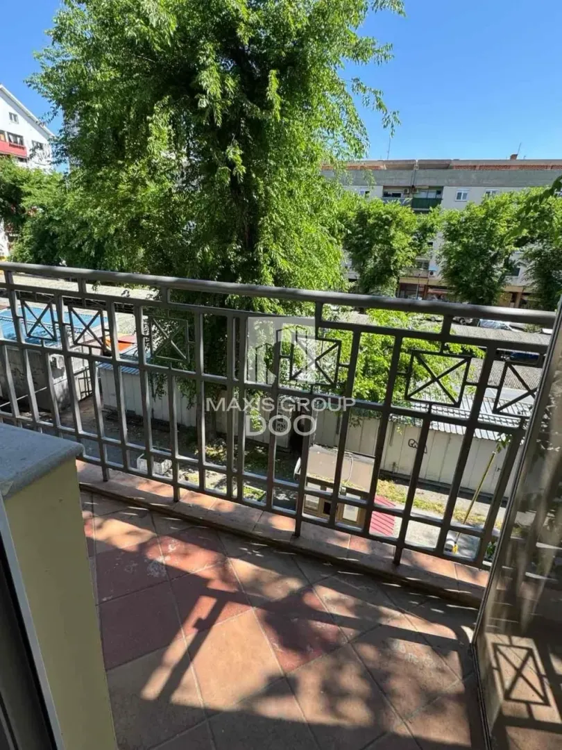Balkon sa metalnom ogradom i pogledom na zelenilo i okolne zgrade.