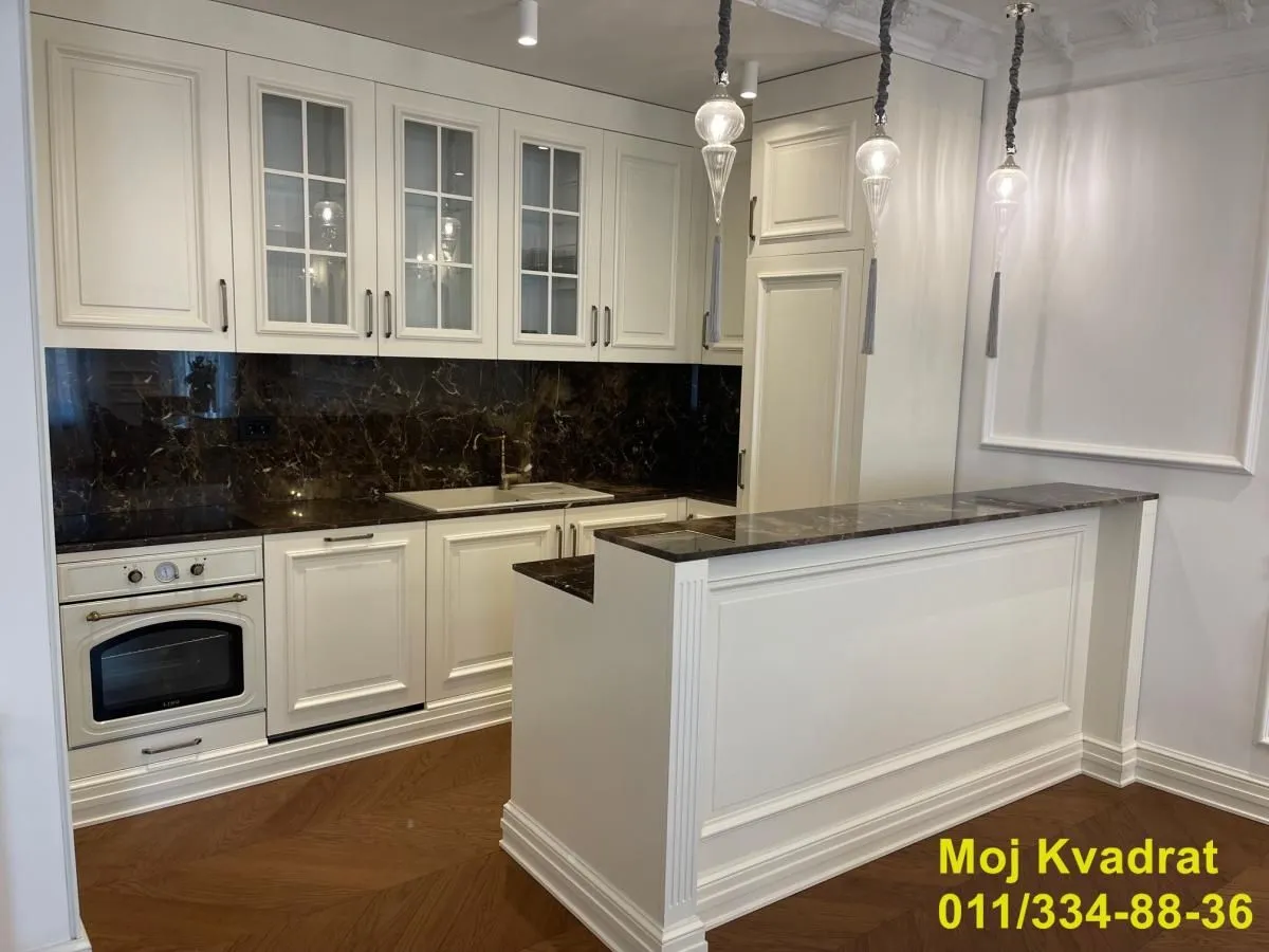 White classic-style kitchen with dark marble countertops and a breakfast bar.