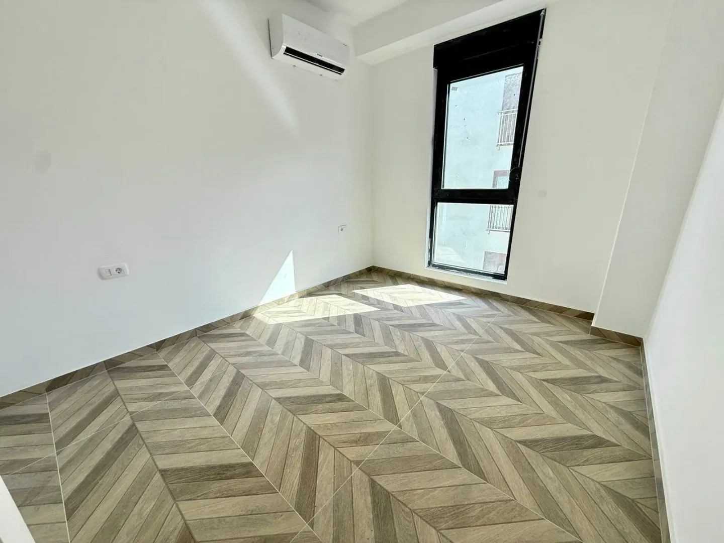 Empty bright room with wooden flooring and an air conditioner on the wall.