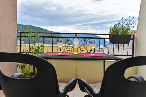 Furnished balcony with a table, two chairs, a bottle of wine, and glasses overlooking the sea and hills. - image 9
