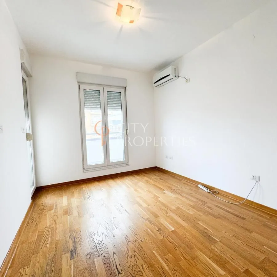 Empty room with wooden flooring, air conditioning unit, and a window.