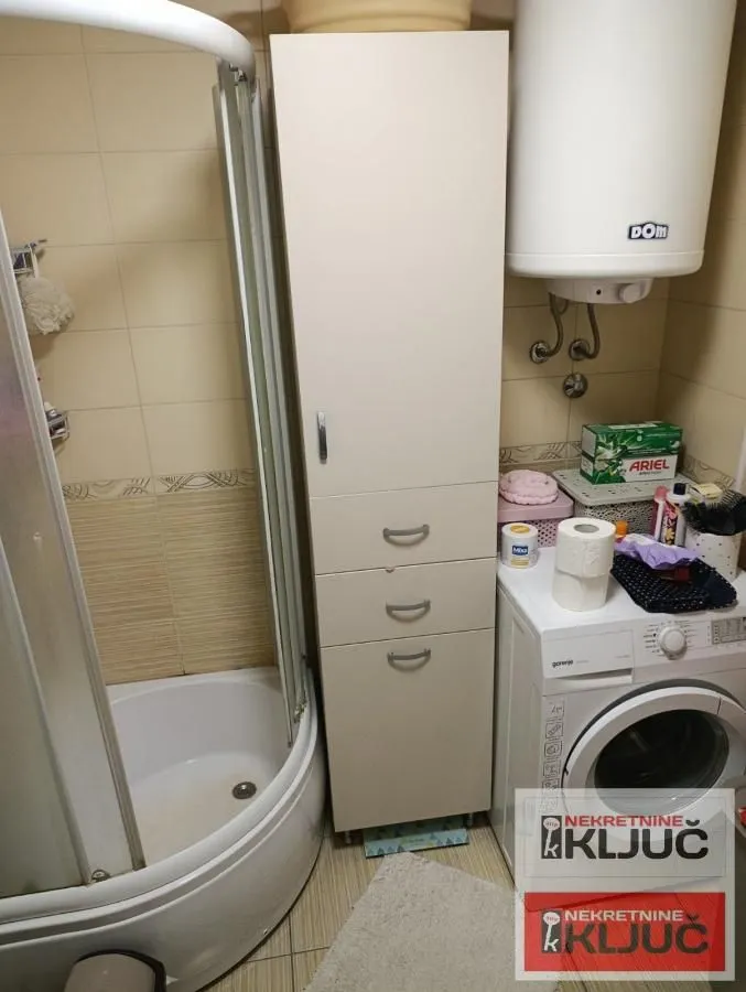 Pogled na kupatilo sa tuš kabinom, ormarićem i mašinom za veš.