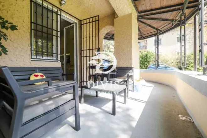 Covered terrace with seating furniture and metal window grilles.