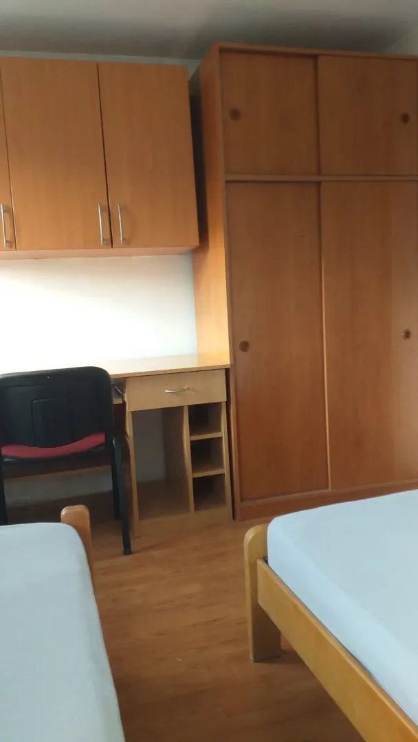 A room with two beds, a study desk, and a wooden wardrobe.