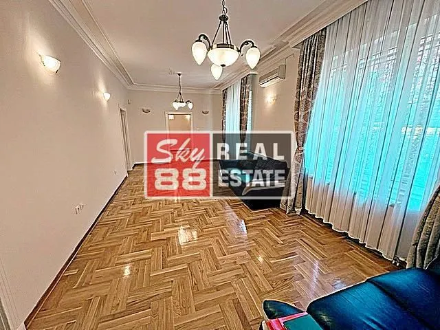 Spacious living room with parquet flooring, sofa, and large windows with curtains.