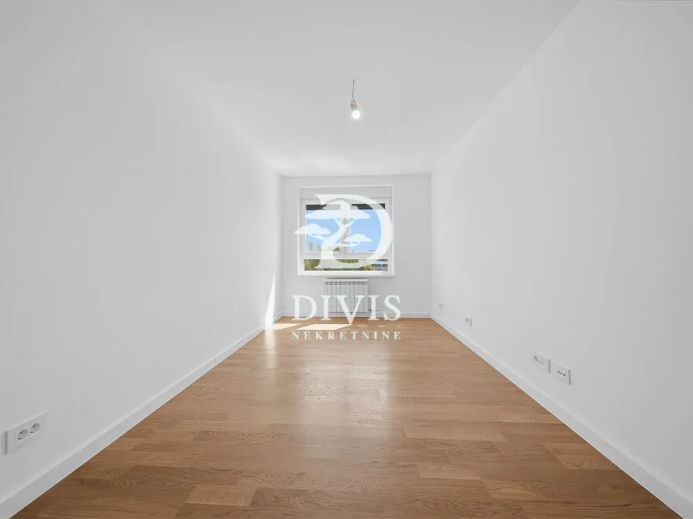 Empty room with white walls, parquet flooring, and a window at the end.