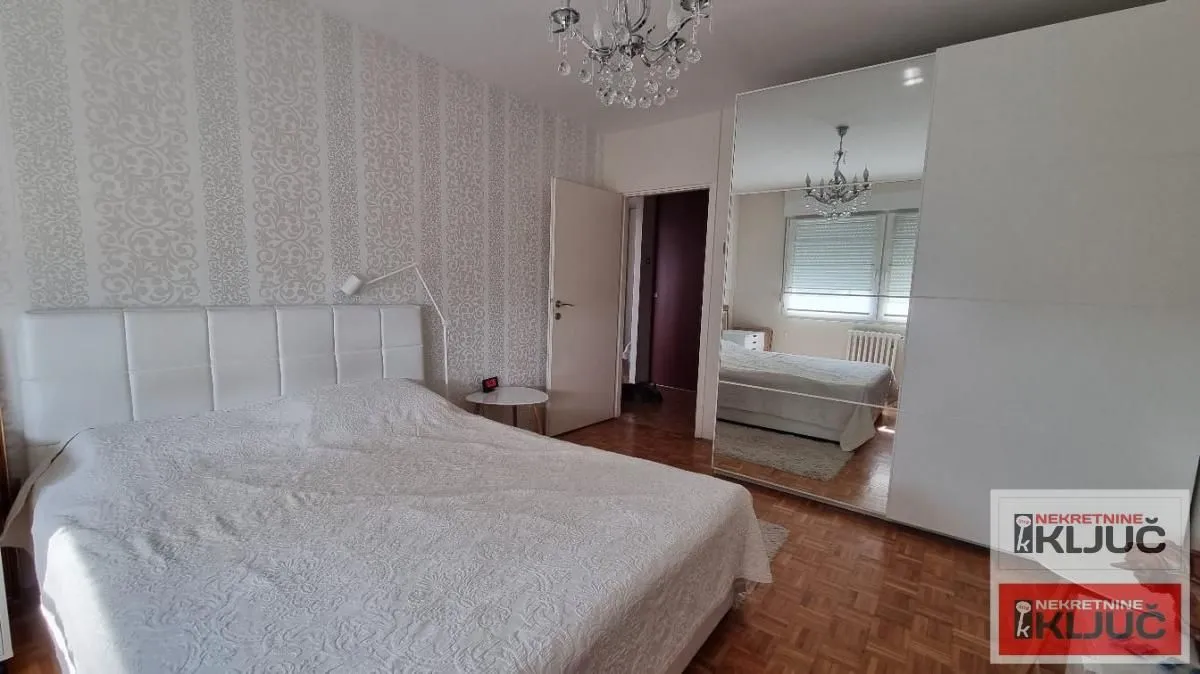Nameštena spavaća soba sa bračnim krevetom i velikim ormarom sa ogledalom.