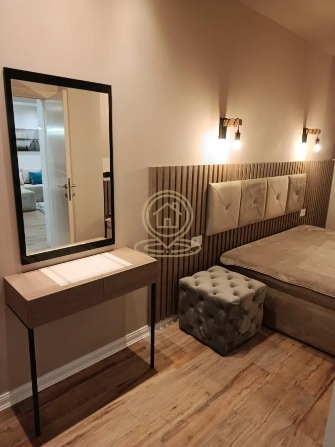 Bedroom with a double bed, upholstered pouffe, and a mirror with a console table.